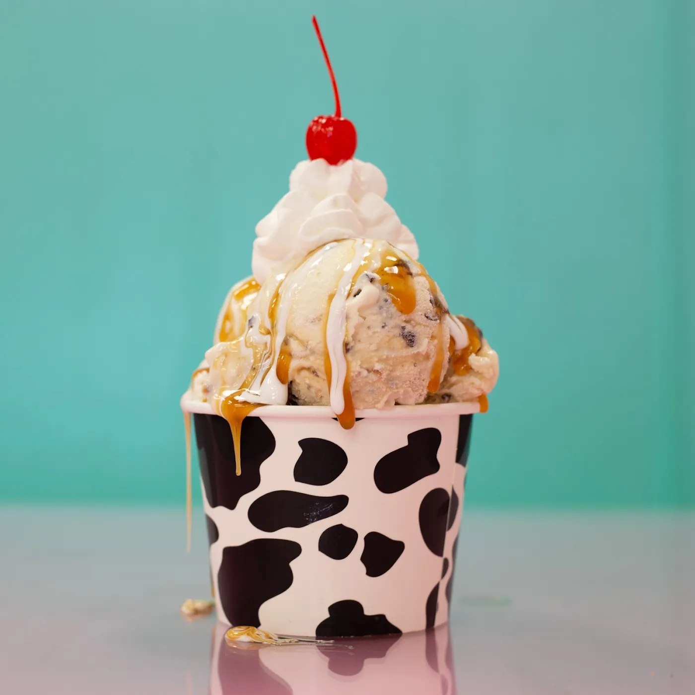 Sundae with whipped cream and a cherry in a cow-print cup on a turquoise background